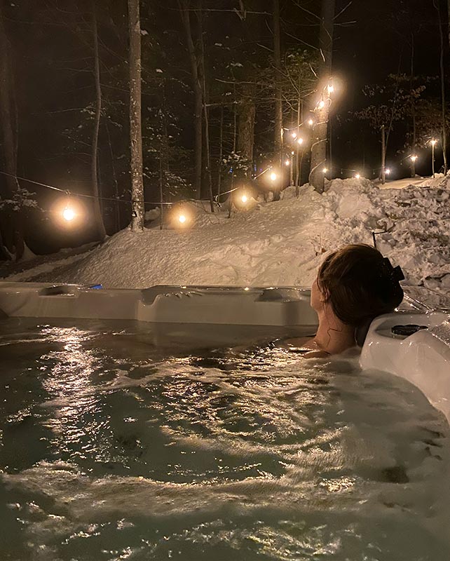 Woman in jacuzzi with winter background and patio lights